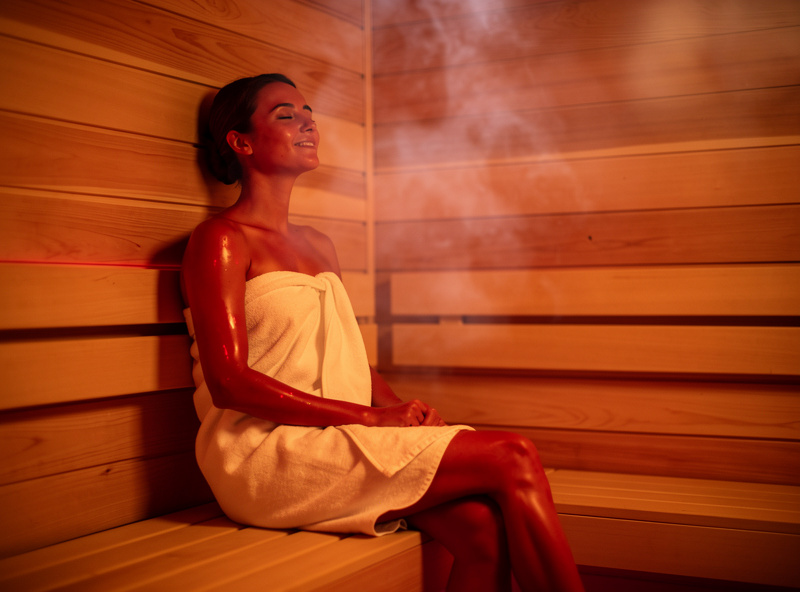 Person relaxing inside a modern infrared sauna with warm red light glow