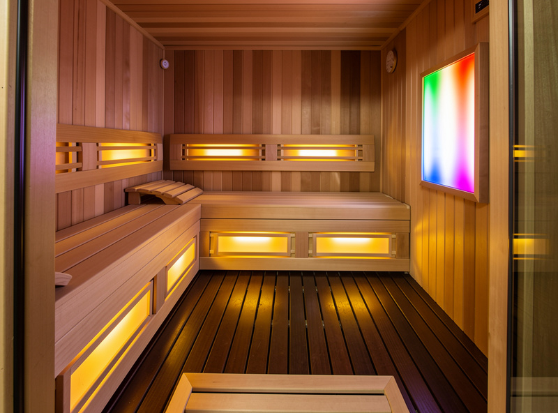 Family-size 4-person infrared sauna cabin in a basement home wellness space with bench seating and chromotherapy lighting