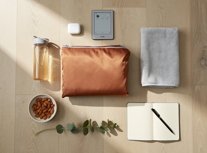 Top-down flatlay of personal infrared sauna routine items including blanket, water bottle, towel, and e-reader
