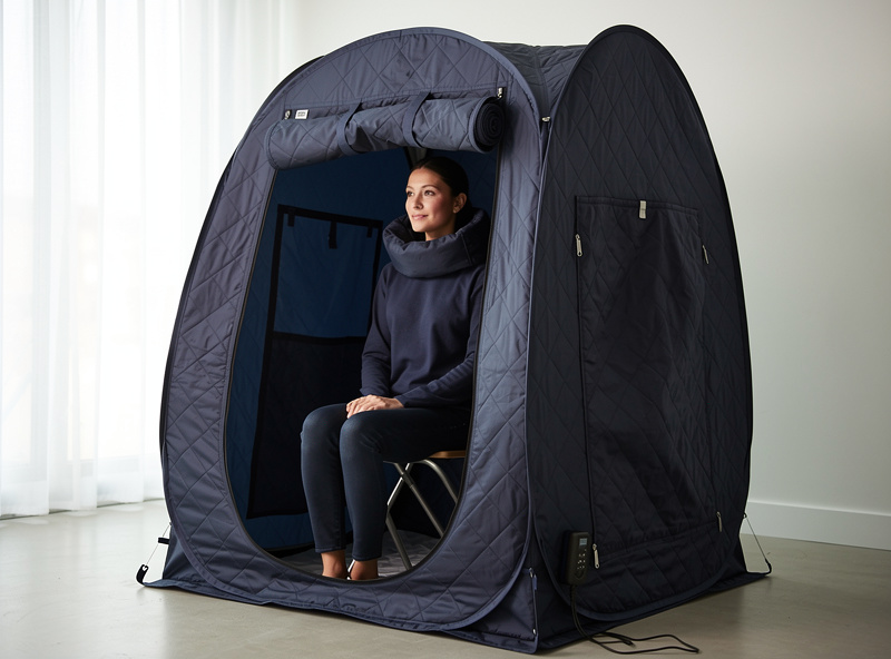 Pop-up infrared sauna tent in dark navy with person seated inside, head out through fabric collar