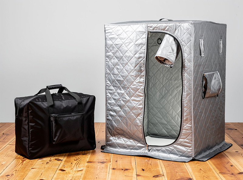 Folded portable sauna tent in nylon carry bag next to assembled version