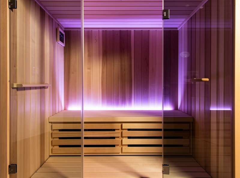 Side view of indoor infrared sauna cabin showing chromotherapy ambient lighting and natural cedar interior