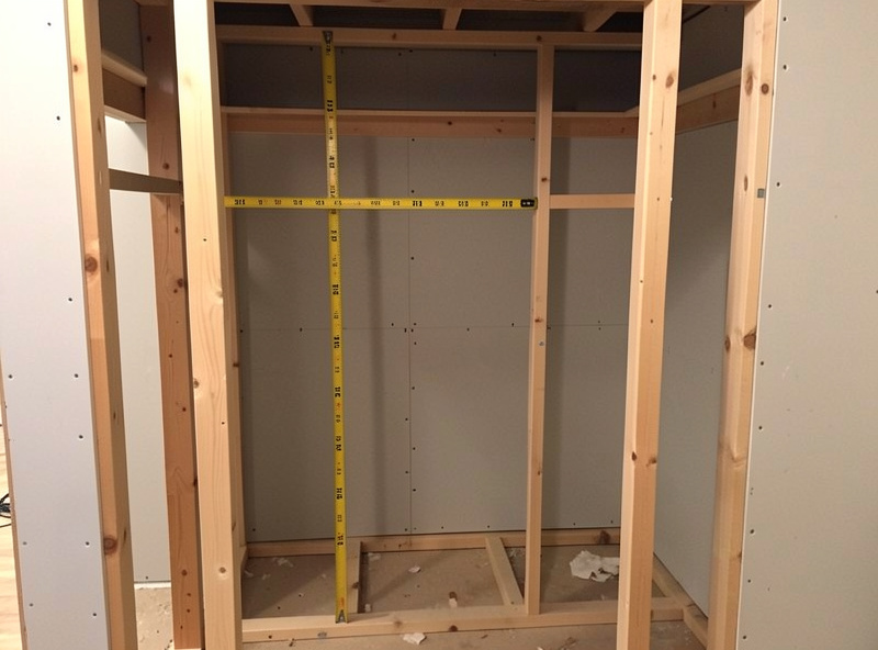 Empty residential closet stripped to studs with a tape measure showing dimensions
