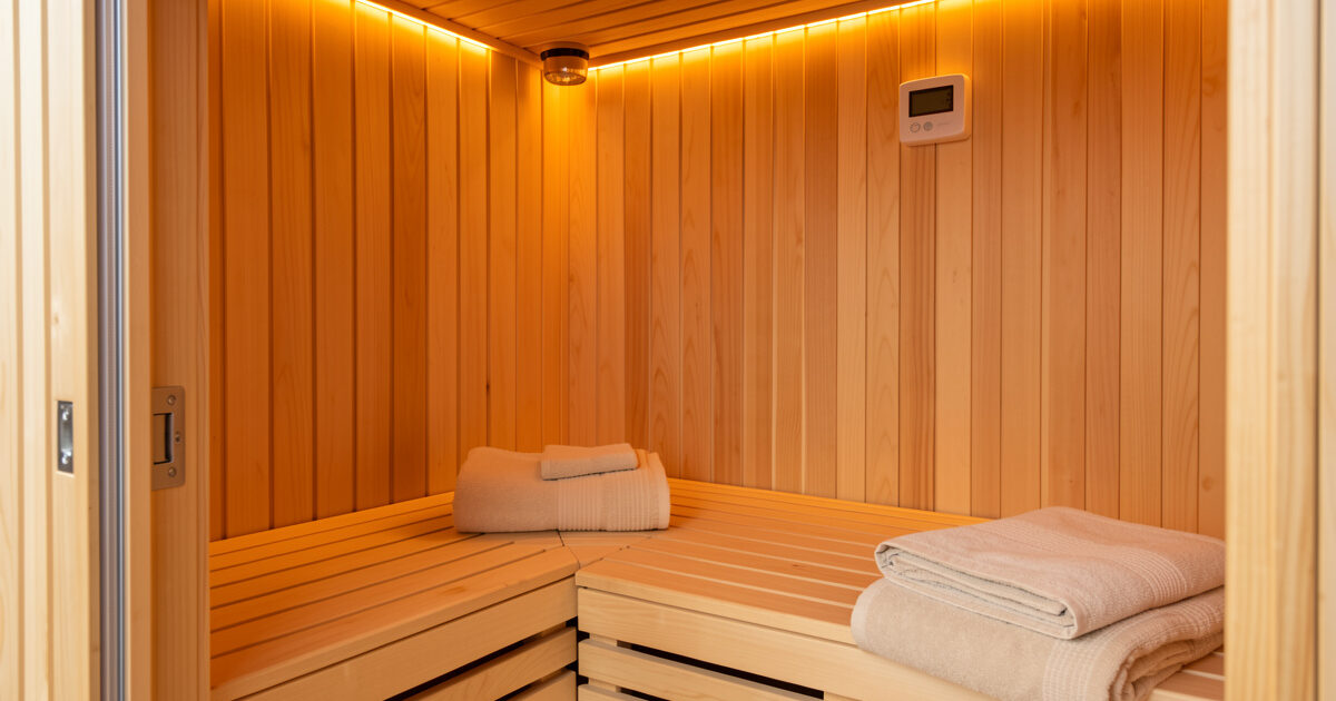 Infrared sauna cabin interior with accessories: amber accent lighting, linen towels, and a wall thermometer