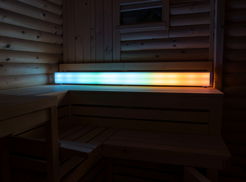 RGB chromotherapy LED light bar glowing above a hemlock sauna bench in a dim cabin