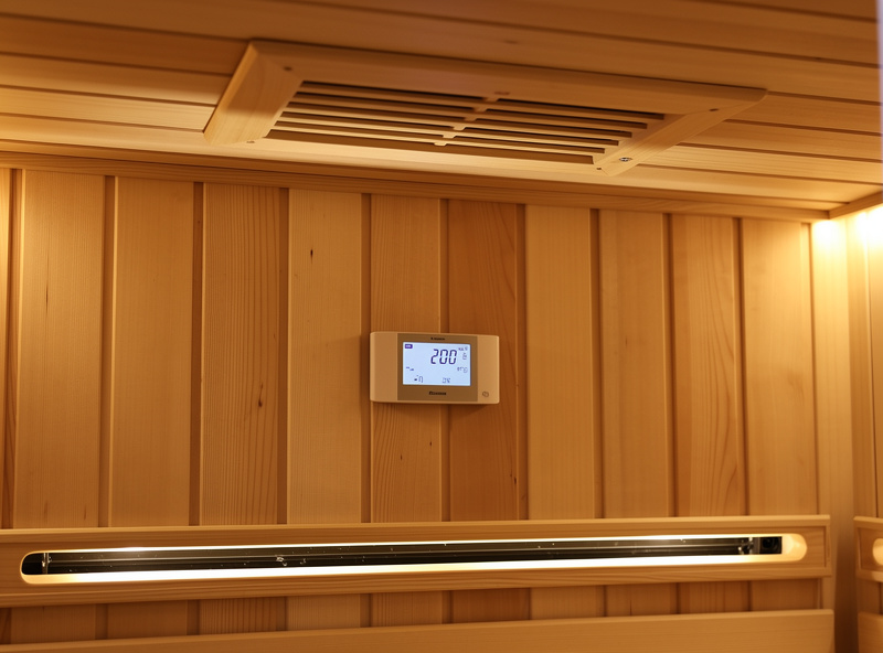 Interior of an infrared sauna showing a ceiling vent and a hygrometer on a hemlock wall