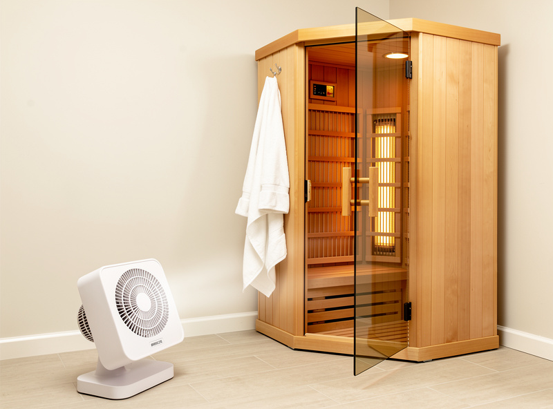 An infrared sauna with its door propped open and a small fan drying it out after a session