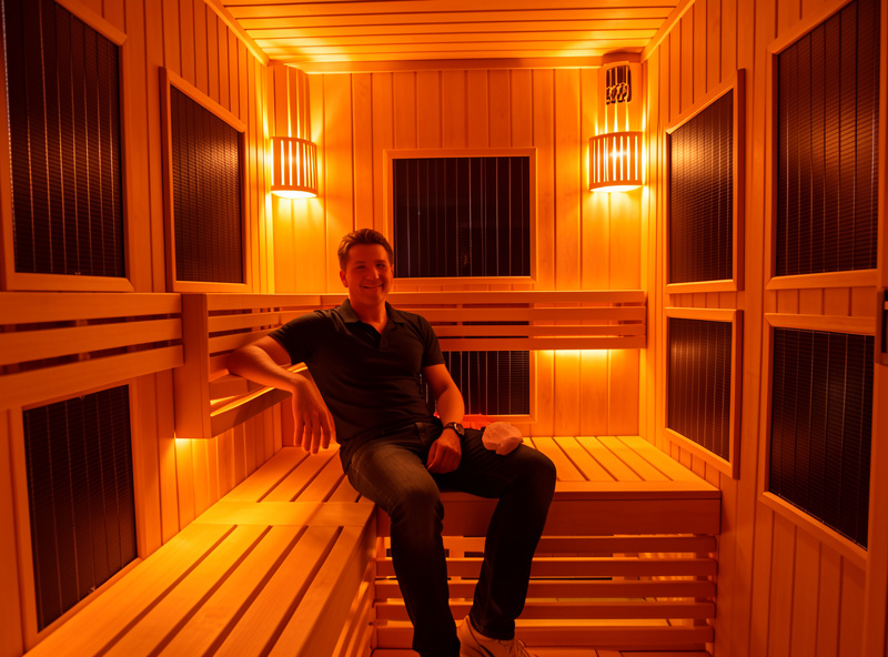 Person seated inside a far-infrared cabin showing even all-around warmth versus directional panel heat