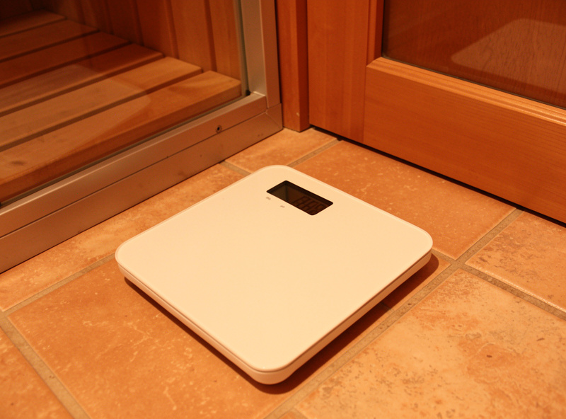 Digital bathroom scale on a tiled floor beside an infrared sauna door