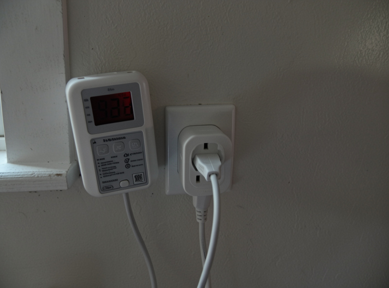Plug-in energy meter and smart plug wired to an infrared sauna power cord on a dedicated circuit in dim winter light