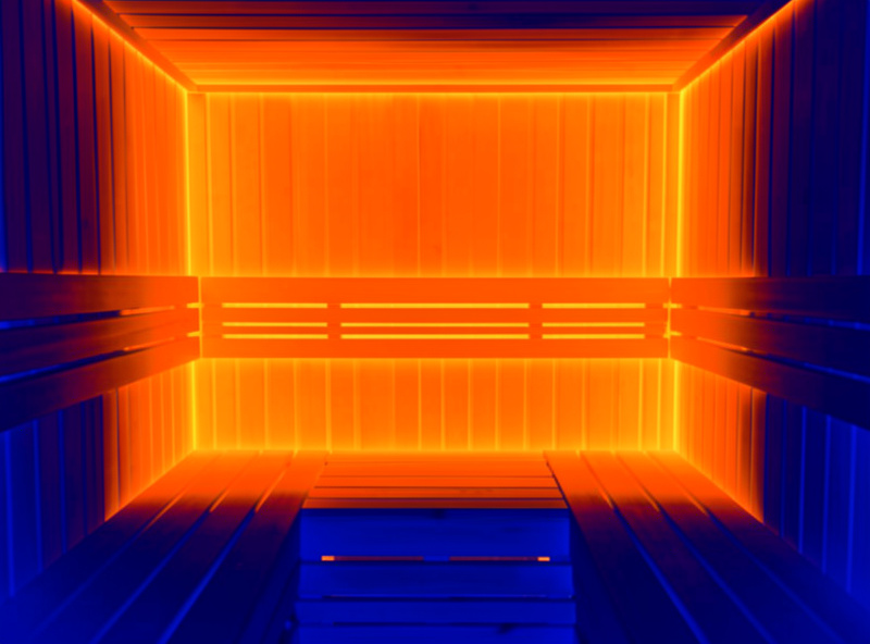 Thermal-imaging false-color view of a two-person sauna interior showing warm panel zones and cooler shaded areas where seats block heat