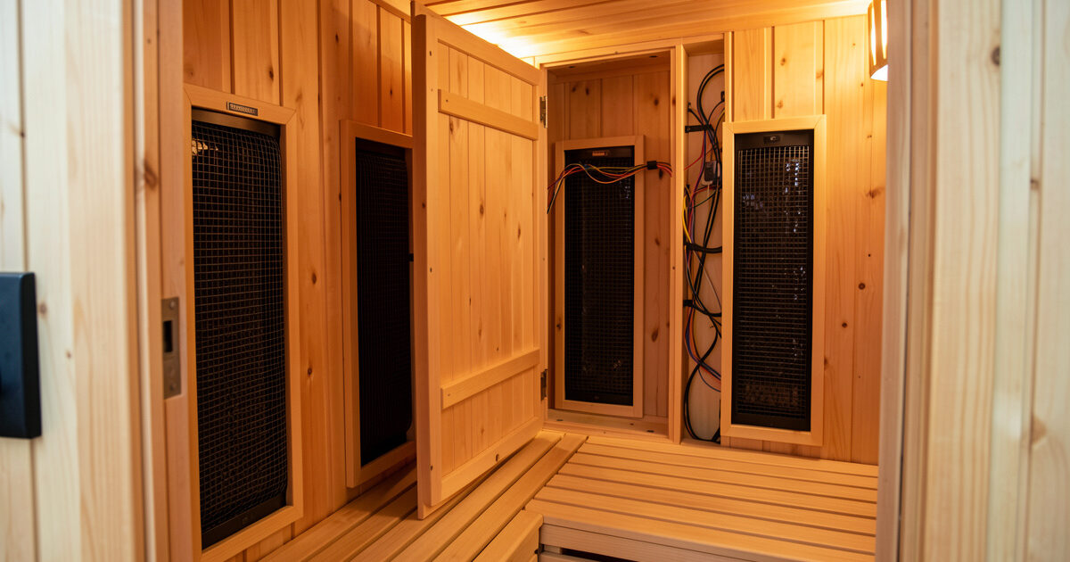 Interior of a far-infrared sauna cabin with an access panel open revealing heater wiring during troubleshooting