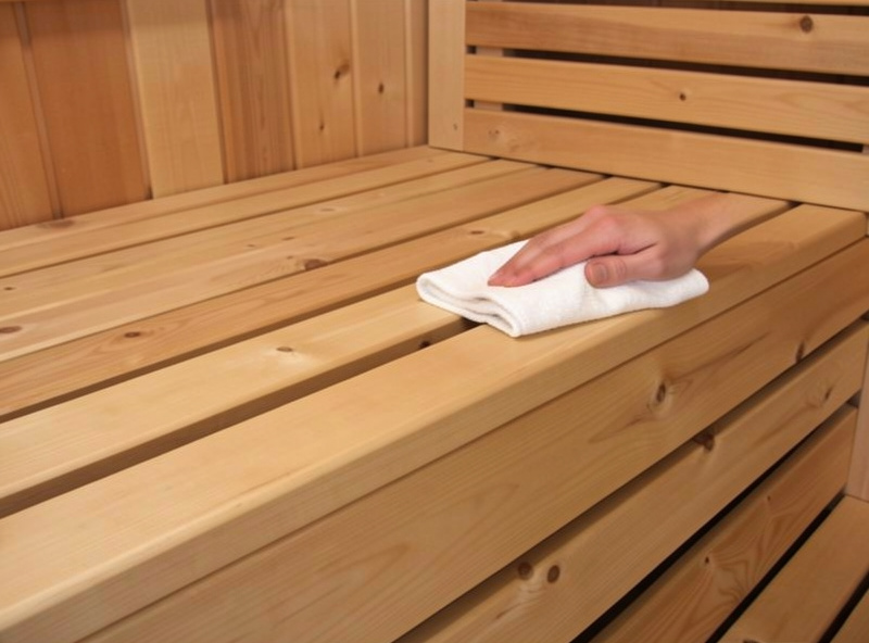 Applying food-safe wood oil to a hemlock sauna bench with a cloth after cleaning