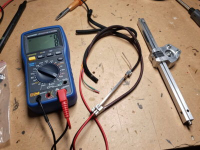 A multimeter and a disconnected infrared sauna heater element on a workbench ready for continuity testing