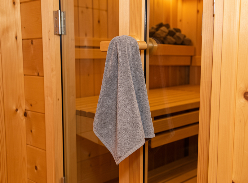 A folded grey microfiber cloth hanging on the glass door handle of a hemlock sauna cabin